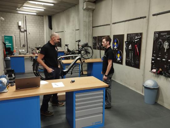 Twee mannen zijn in gesprek in een werkplaats voor fietsherstellingen.